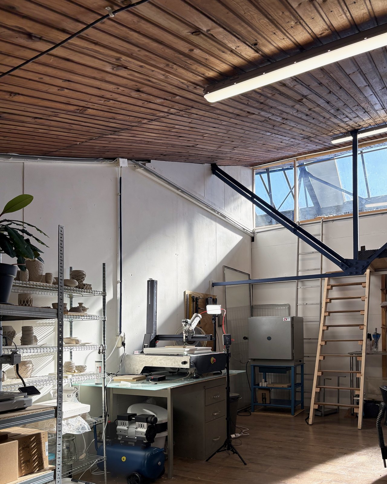 The studio under the skylight: the clay printer on its desk, a shelf of printed pieces, the kiln and a ladder to the mezzanine